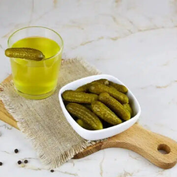 Pickled dills in a bowl and pickle juice in a glass.
