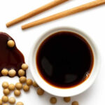 Soy sauce in a bowl and chop sticks and few soy beans.