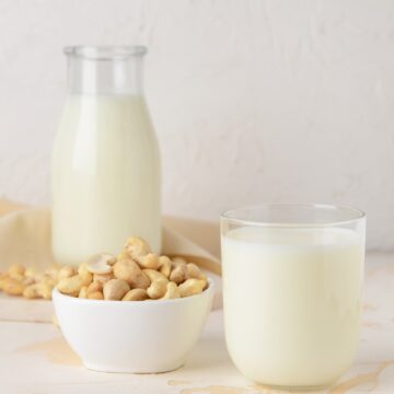 A glass and a bottle of cashew milk and a bowl of cashews.