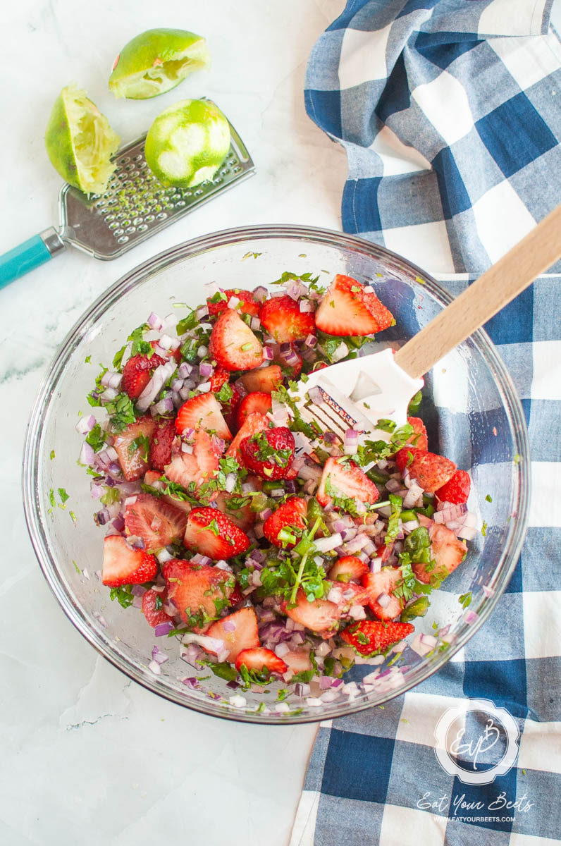 diced strawberries and red onion in a dish with limes wedges on the side.