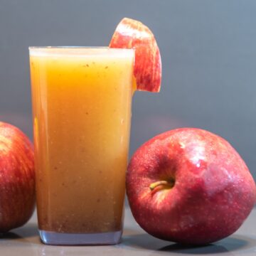 apple juice in a glass and a whole apple on side.