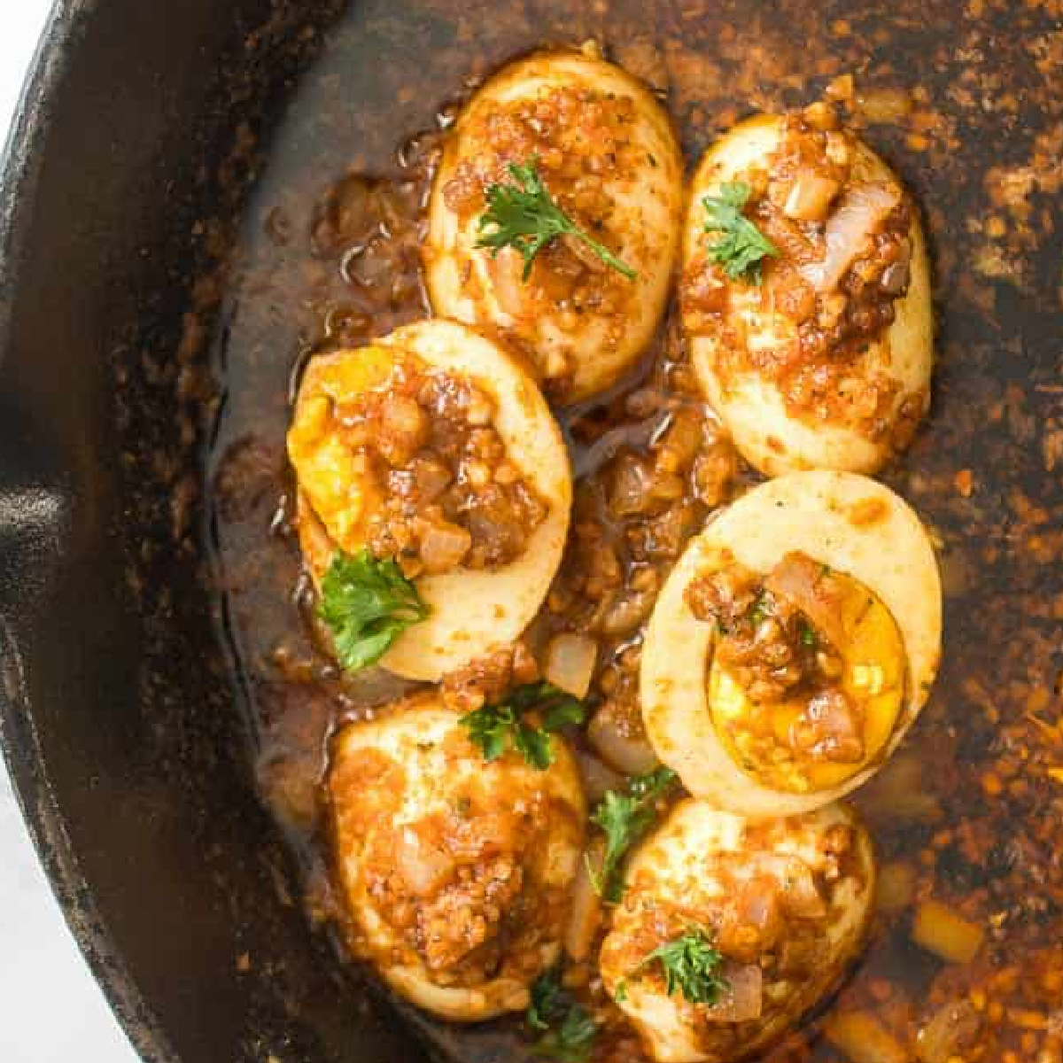 tik tok egg boil in a skillet. six eggs covered in a spicy sauce and garnished with herbs.