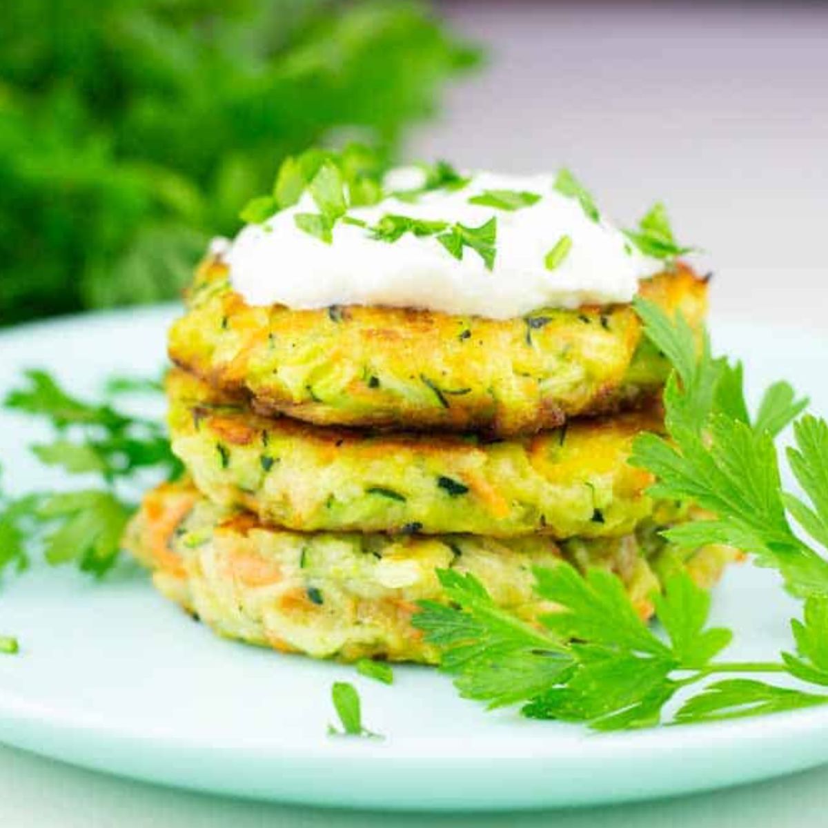 Air Fryer Zucchini Fritters piled on a plate and topped with sour cream and herbs.