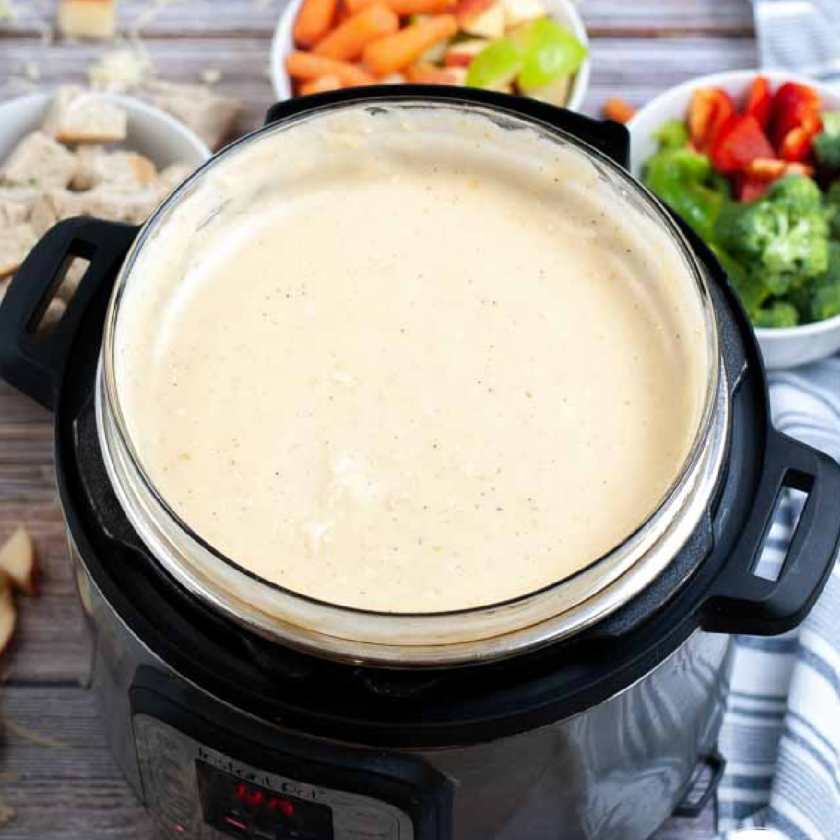creamy cheese fondue in an instant pot surrounded by crunchy vegetables in bowls.