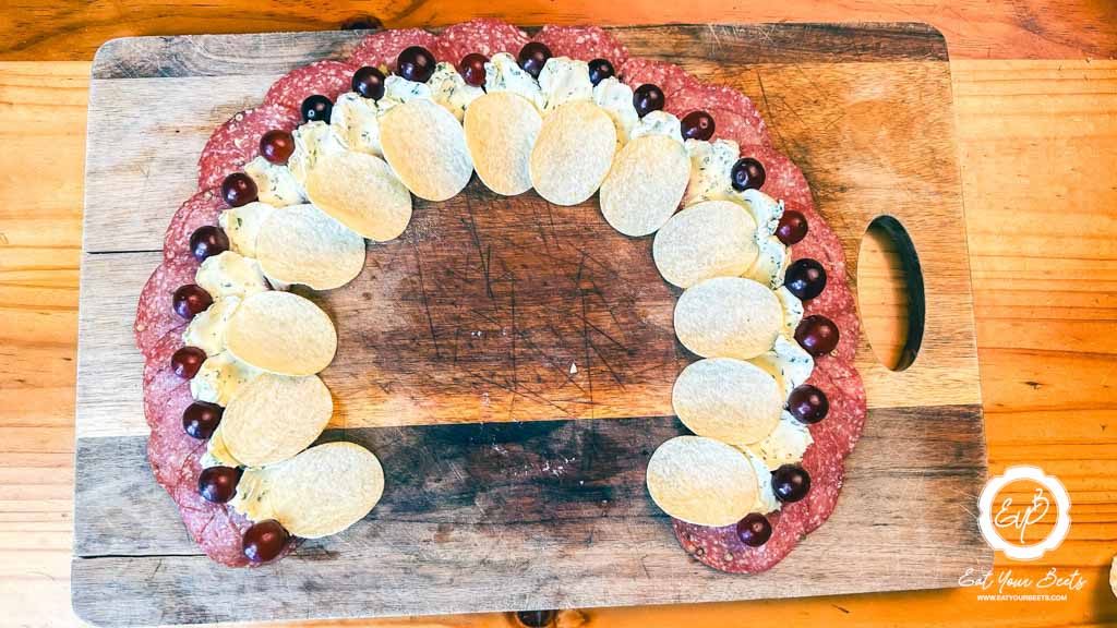 Decorating pepperoni, cream cheese, grapes, pringles on wooden board.