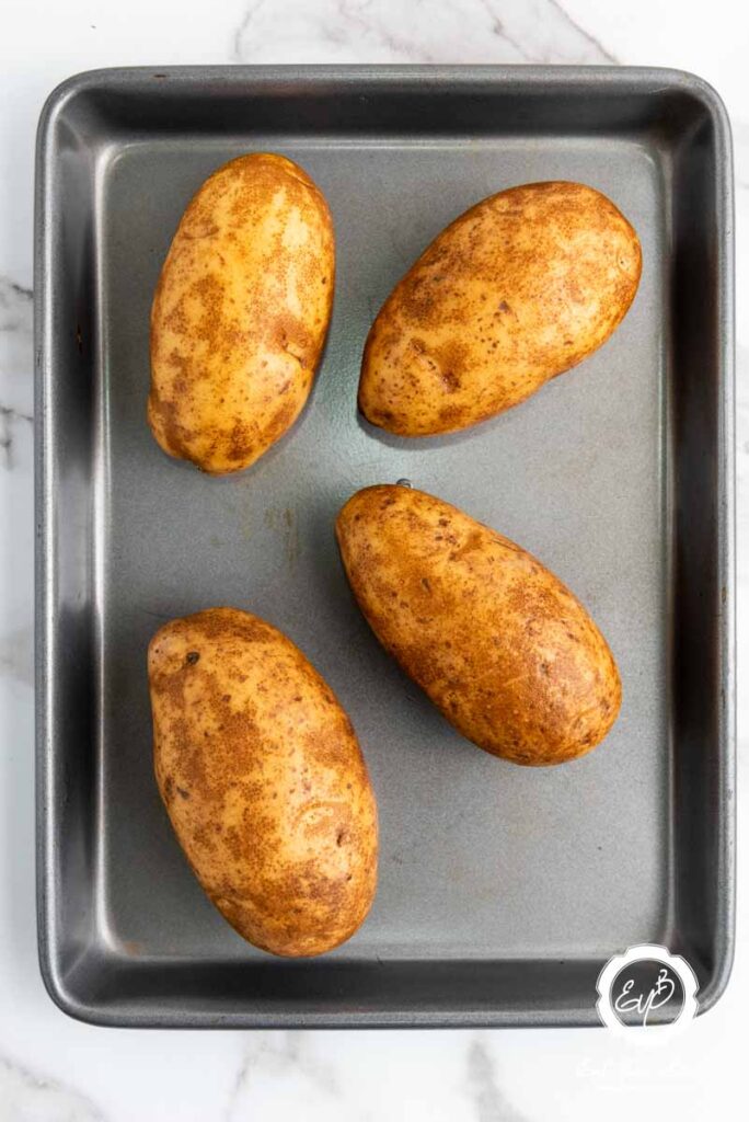 four potatoes on a baking sheet.