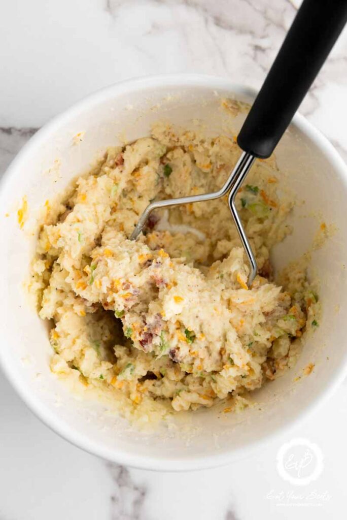Mashing potatoes with sour cream, cheese, bacon, and seasonings.