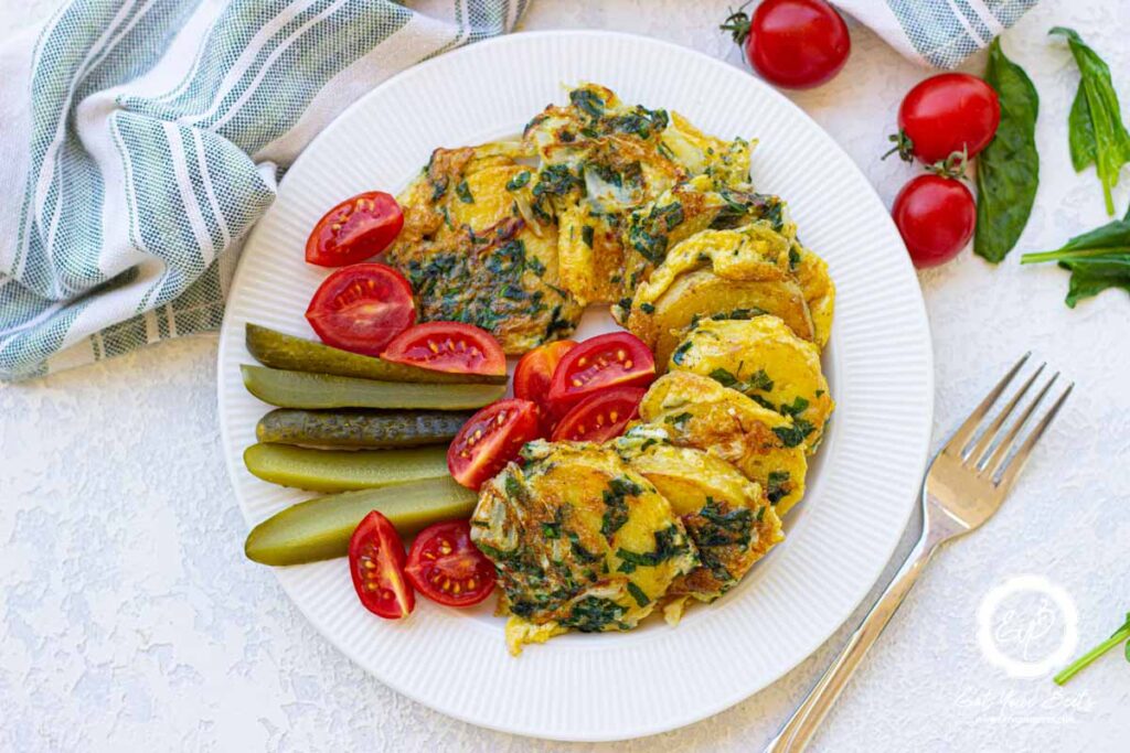 spinach and cabbage potatoes on plate with a side of tomatoes and pickled cucumbers.