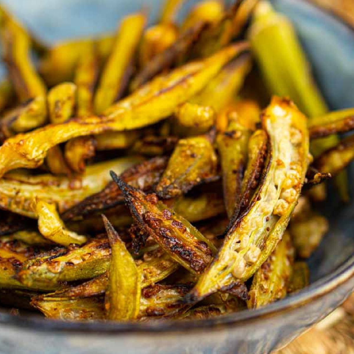 Crispy air fried Okra Chips in a blue bowl sprinkled with paprika. 
