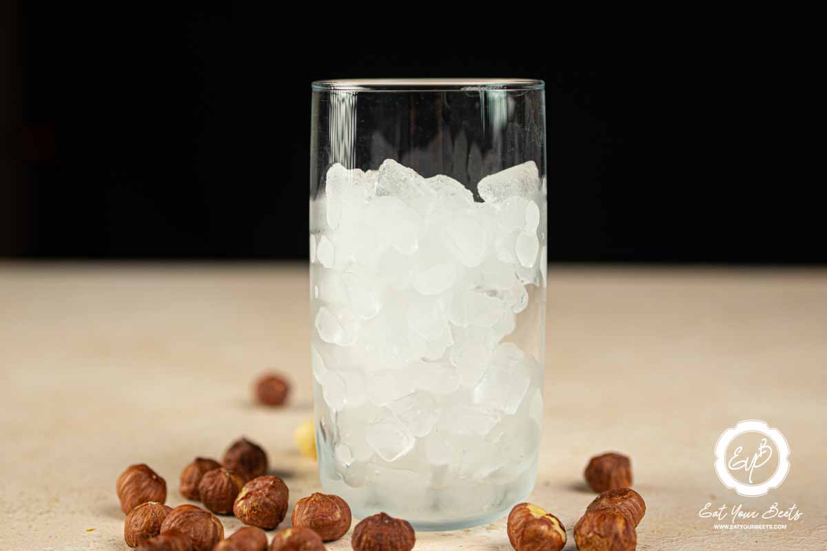 Ice in a glass and hazelnuts on side.