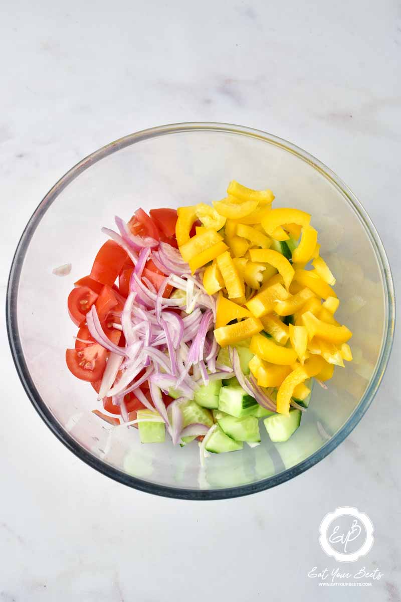 Chopped cucumber, bell pepper, onion, and tomatoes in a bowl.