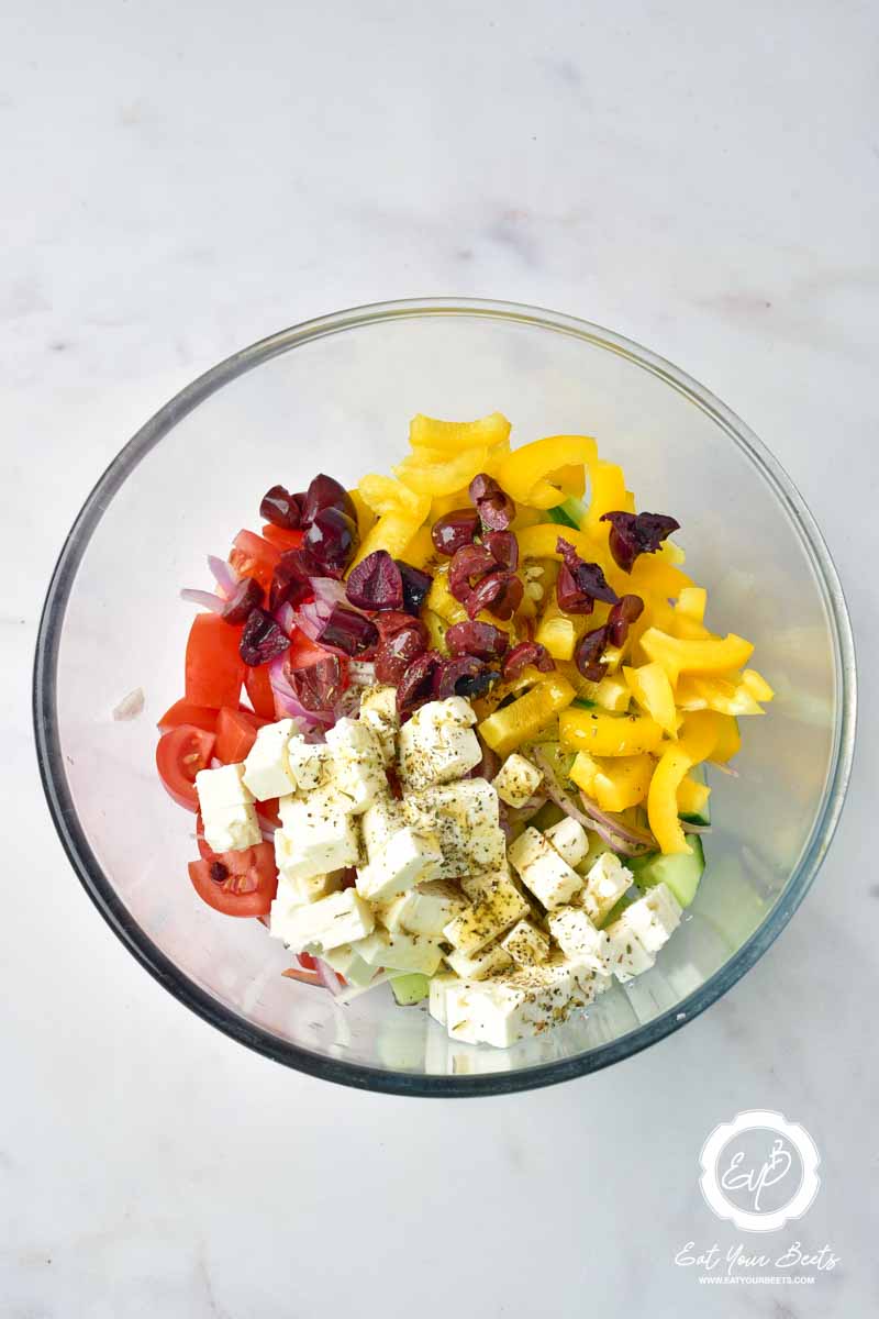 Cubed feta cheese, chopped cucumber, bell pepper, onion, , olives, and tomatoes in a bowl.