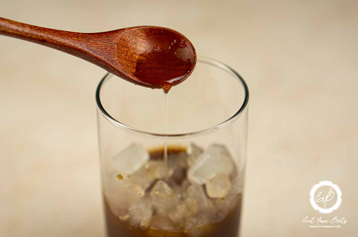Pouring hazelnut syrup in a glass of brewed coffee.