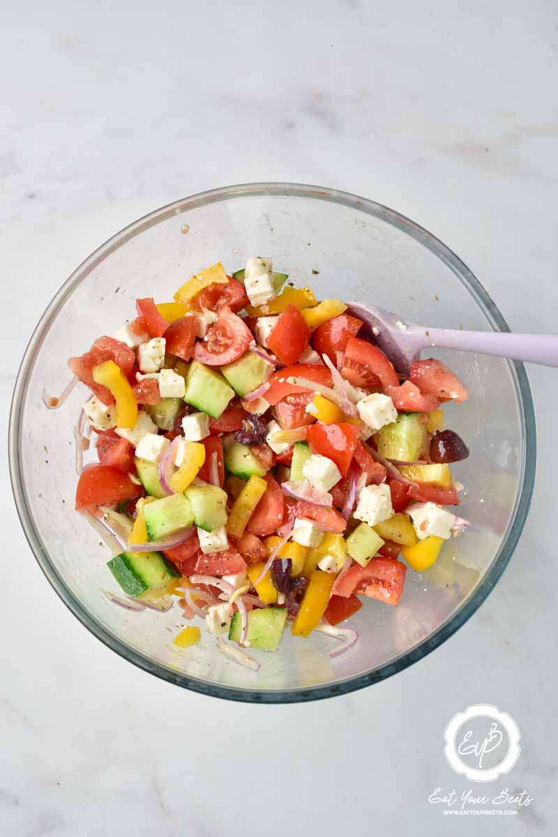 Mixing chopped veggies and feta cheese with spices infused vinegar.