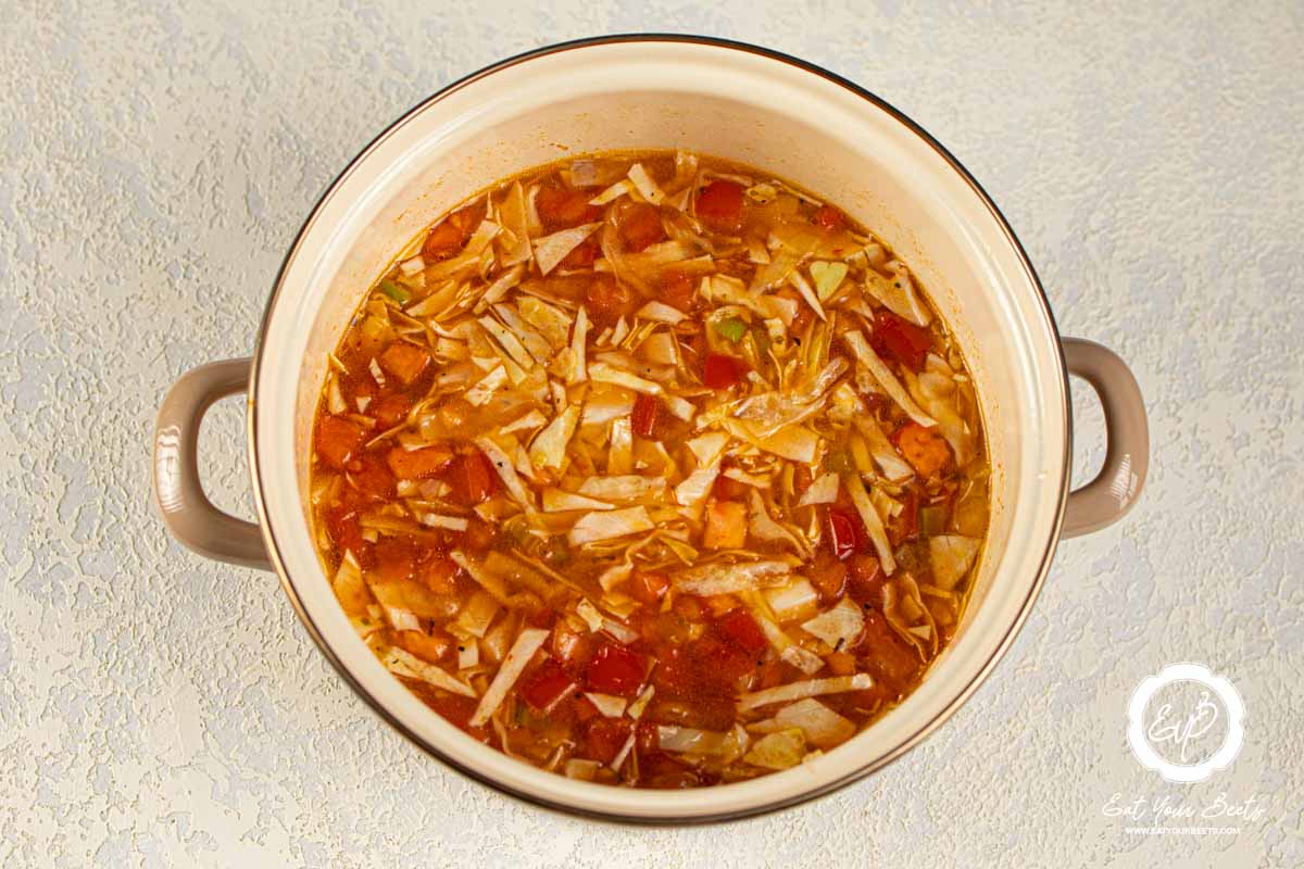 Cooking onions, garlic, carrots, and celery with canned tomatoes in a pan.