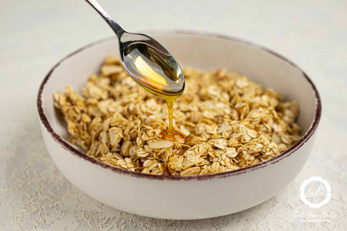 Pouring honey over Oats, almonds, walnuts, and sesame seeds.