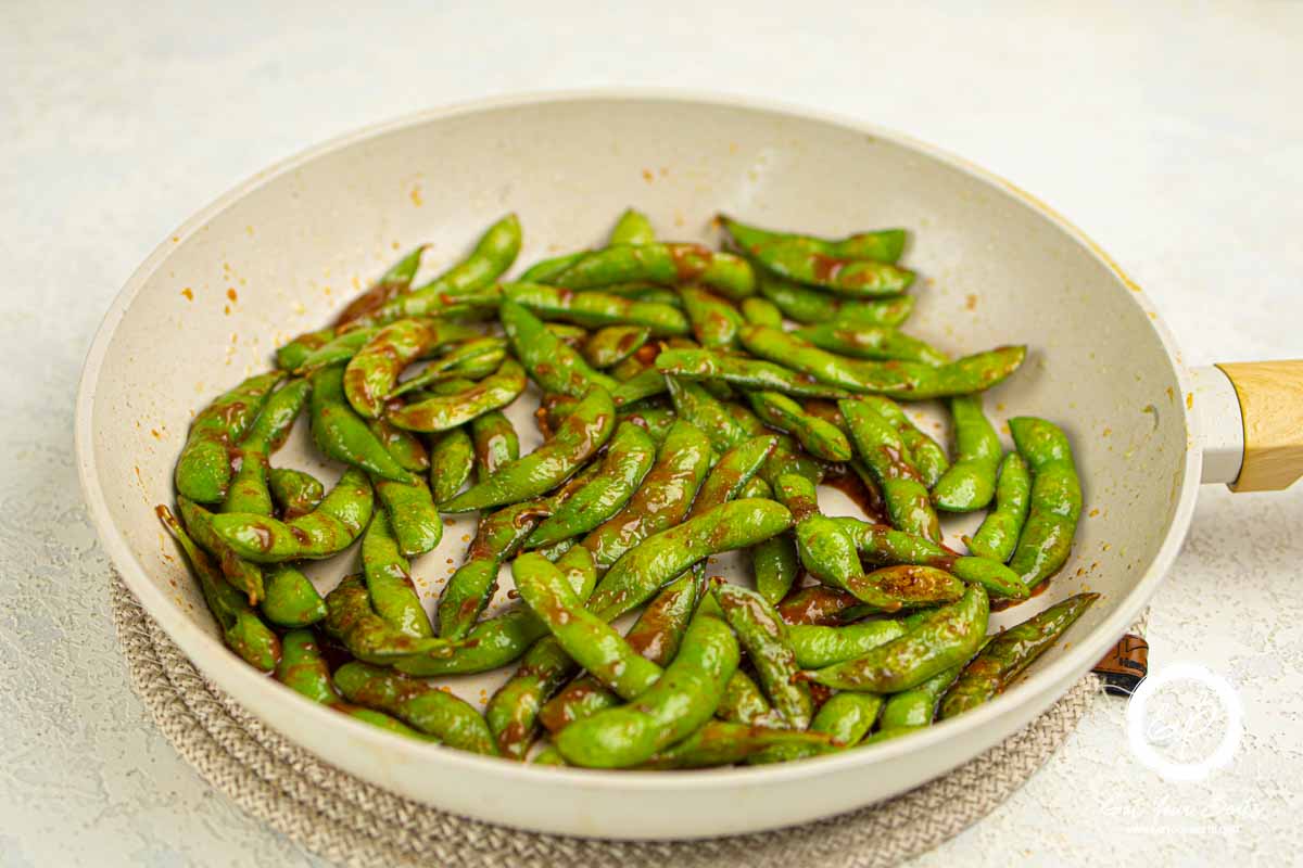 Chili sauce coated edamame in a pan.