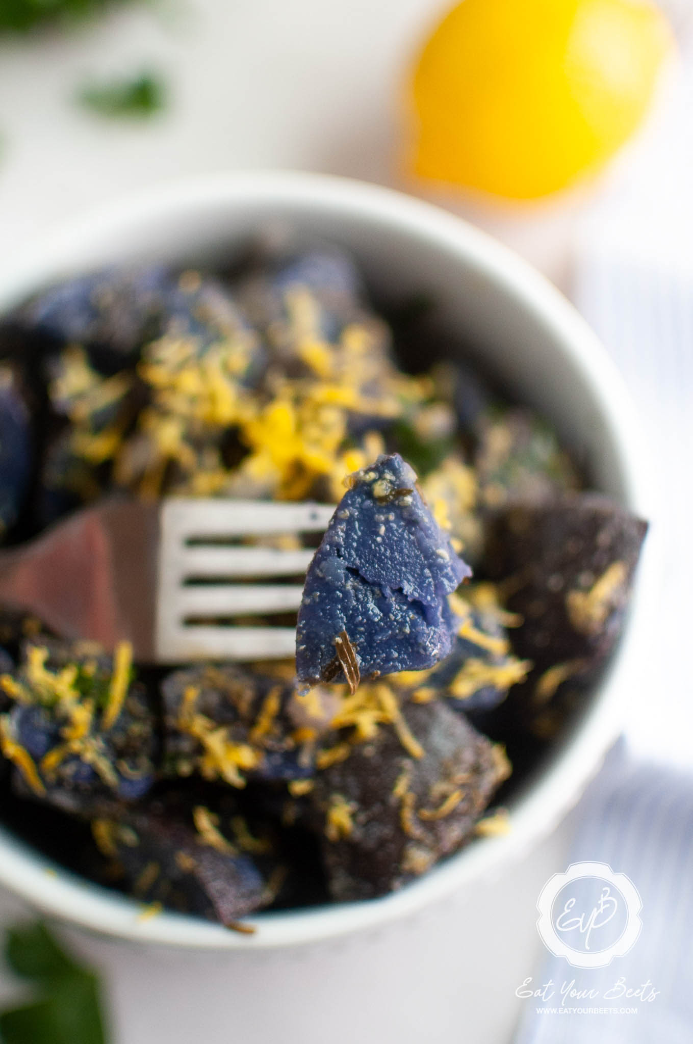 purple potato on a fork, over a potato salad with lemon zest.