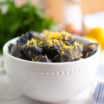 Purple Potato Salad in a white bowl garnished with parsley chives and lemon zest.