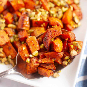 roasted harissa sweet potatoes on a plate, drizzles with honey and pistachio nuts.