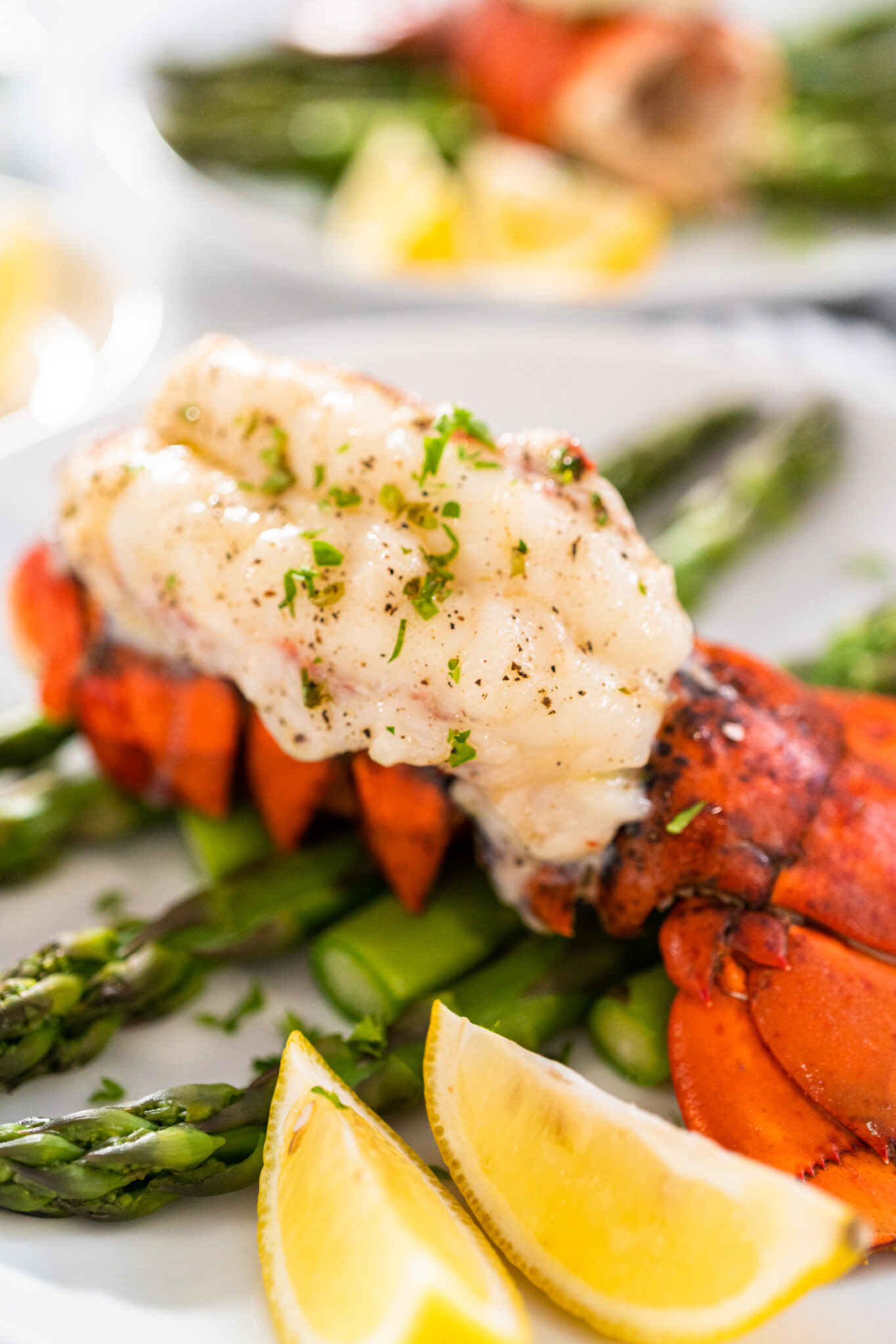 Sering garlic lobster tails with steamed asparagus and lemon wedges on a white plate.