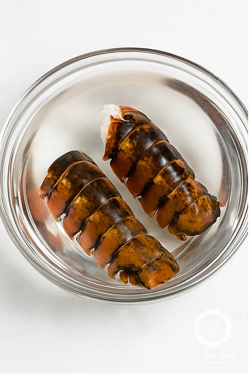 defrosting lobster tails in a glass bowl with water.