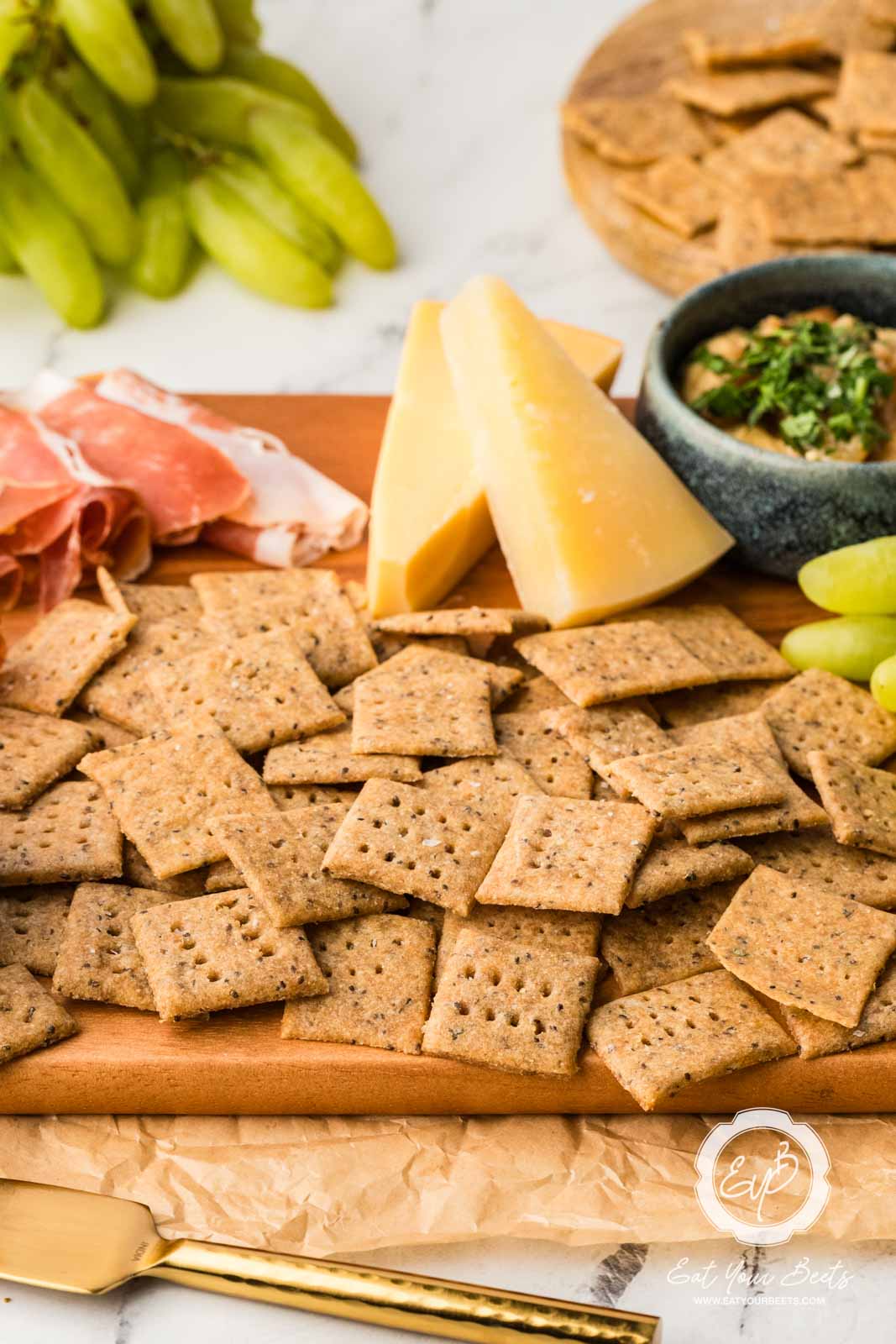 Einkorn Crackers on a cheeseboard with block of parmesan cheese and dip.